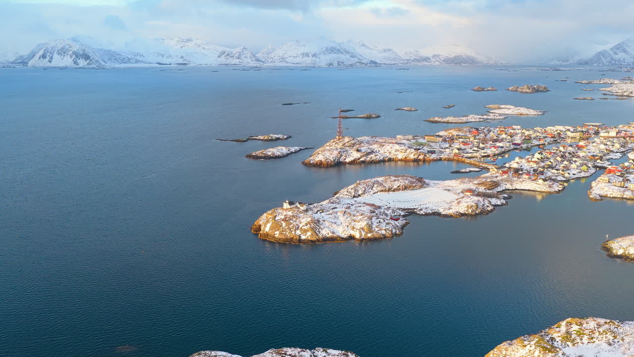 Una impresionante toma cinematográfica con dron del nevado pueblo pesquero de Henningsvaer en Lofoten, Noruega, rodeado de aguas árticas azules y montañas durante la hora dorada