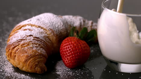 glass of milk being poured next to strawberry and croissant