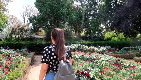 Caucasian-brunette-young-woman-walking-happily-in-garden-with-lot-of-flowers-at-sunny-day