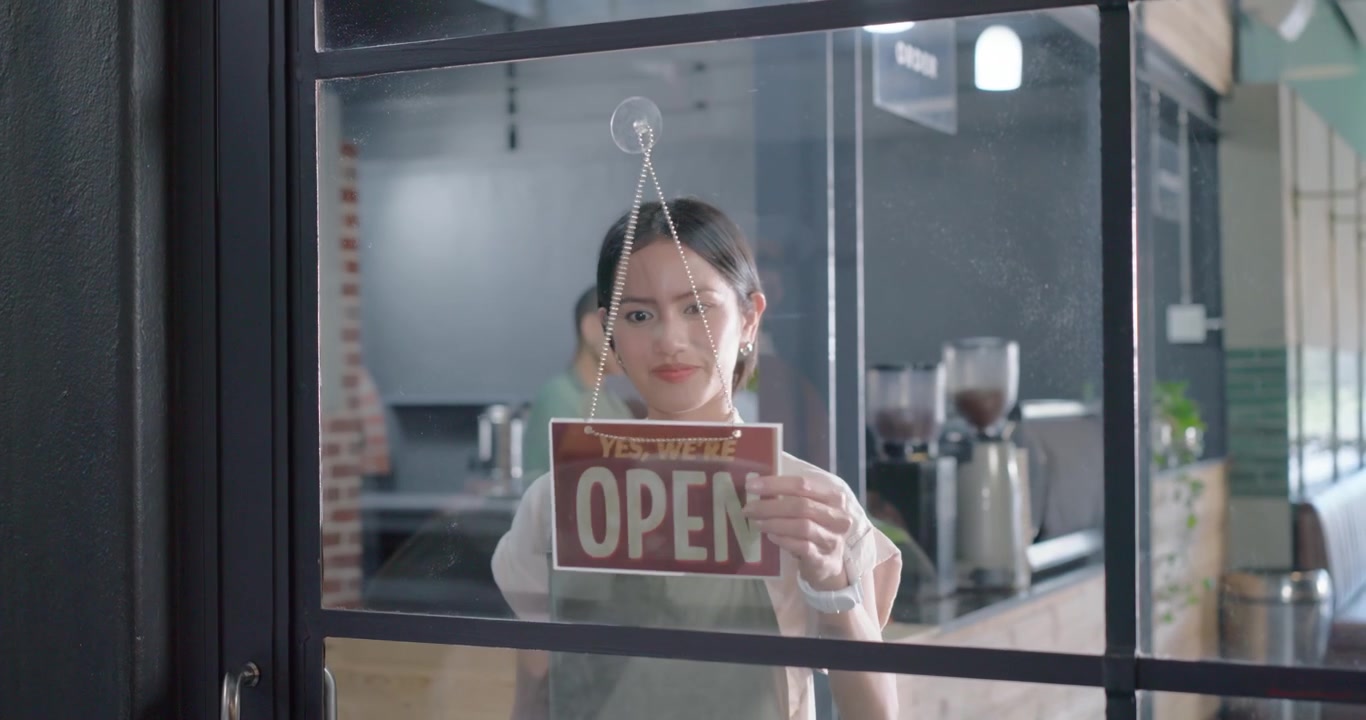 Personale femminile vario vicino alla macchina del caffè che vede il barista girare il cartello "chiuso", aprendo la porta per aprire la caffetteria.