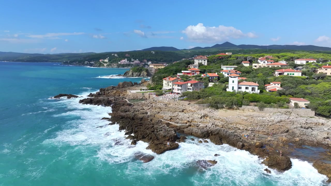 Splendida rivelazione aerea rotante di case private al largo di una spiaggia rocciosa con onde frangenti al largo a Castiglioncello, Italia