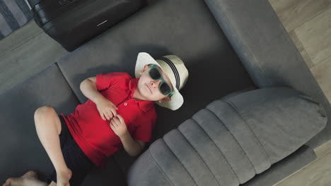 sweet toddler in hat puts hands behind head lying on sofa