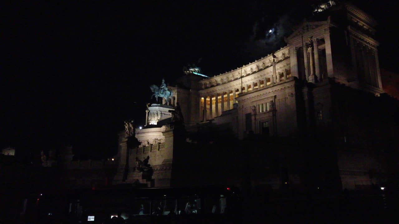 4K video of the Altare della Patria. One of the biggest roman building in the Italian capital. Many vehicles are passing by. The moon shows up in the scene behind the building.