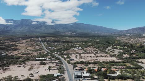 Aerial-View-of-a-Scenic-Road-Through-a-Small-Town-and-Mountains