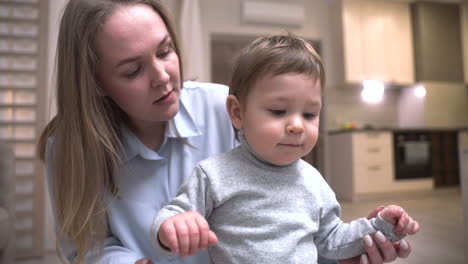 mother holds her baby who is standing on the floor in the living room at home