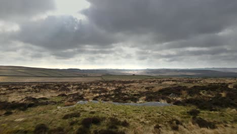 cinematic, aerial drone footage flying over vast open moorland and fields revealing a dramatic skyline and cloudy sky