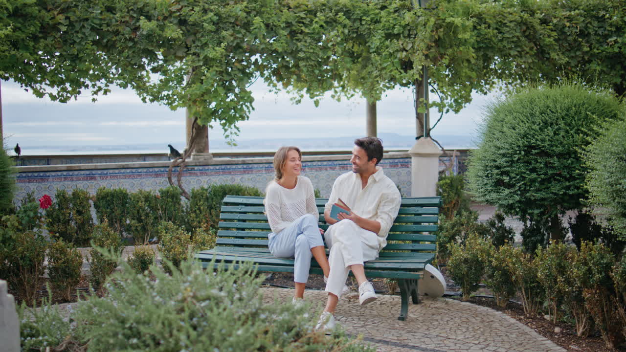 공원 벤치에서 재미있는 책을 읽는 웃는 커플. 데이트에서 여자친구를 포옹하는 남자