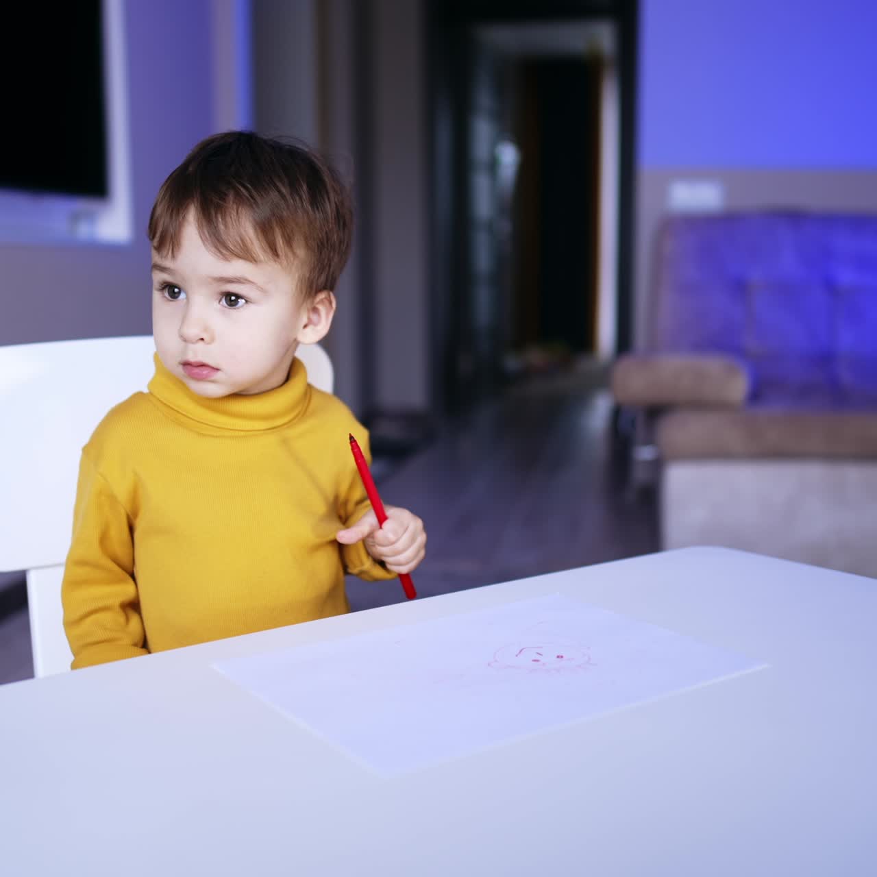 Simpatico bambino che usa un pennarello. Il bambino con il maglione giallo smette di disegnare e guarda attentamente di lato.