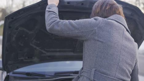 attractive business woman in grey coat opening the car's bonnet and looking under the hood in the street