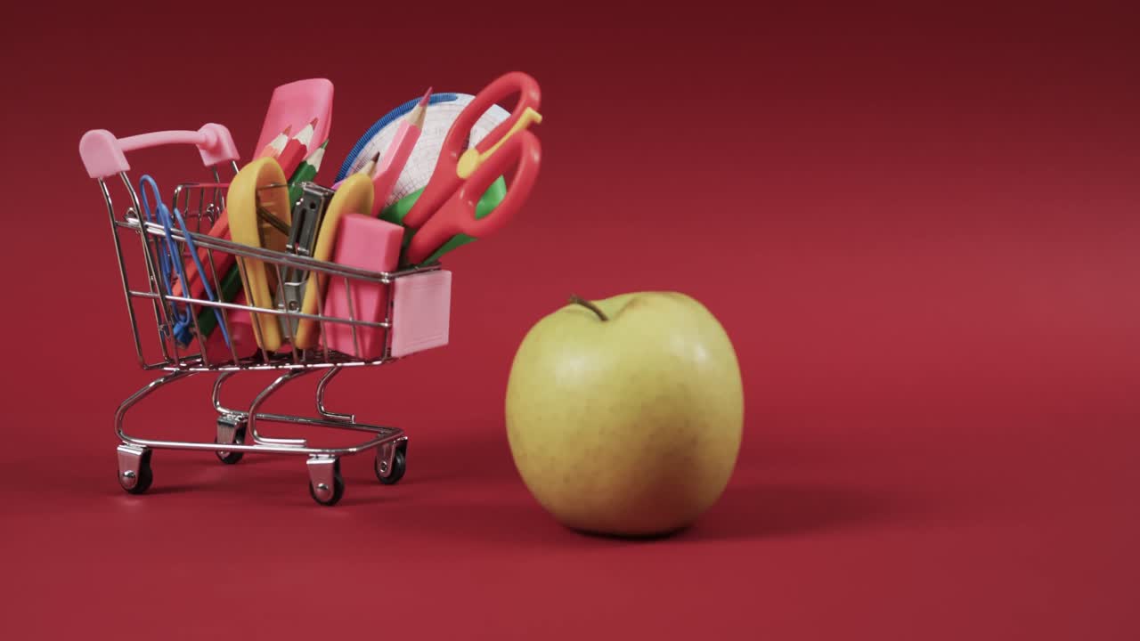 cerrar el carrito de compras con artículos escolares y manzana con espacio de copia en fondo rojo