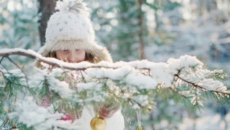 Una-Niña-Con-Un-Sombrero-De-Invierno-Fresco-Decora-El-árbol-De-Año-Nuevo-En-El-Parque-Con-Varias-Bolas