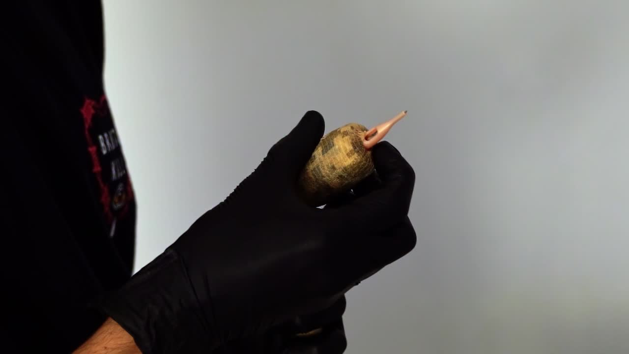 Zbliżenie w zwolnionym tempie, nagrane z ręki, przedstawiające dłoń tatuatora przygotowującego maszynkę do tatuażu na sesję z klientem, poprzez owijanie taśmą w celu stworzenia uchwytu i zakładanie igły.