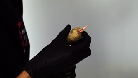 close up slow motion handheld shot of a the hand of a tattoo artist preparing their needle gun tool for a client session by wrapping on tape to create a hand hold and adding the needle