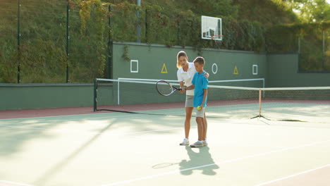 woman teaching his teen son how to play tennis on a summer day 1