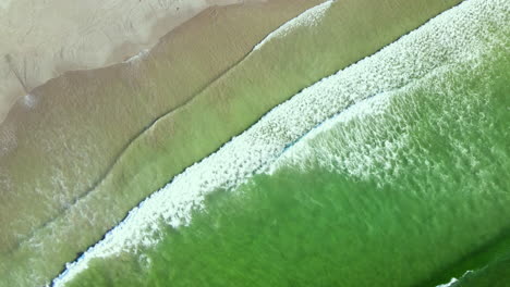 diagonal top drone view as waves run out onto sandy beach from aquamarine ocean