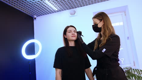 brunette mid-aged woman is in beauty salon. female specialist applies white contour for future permanent make up. low angle view.