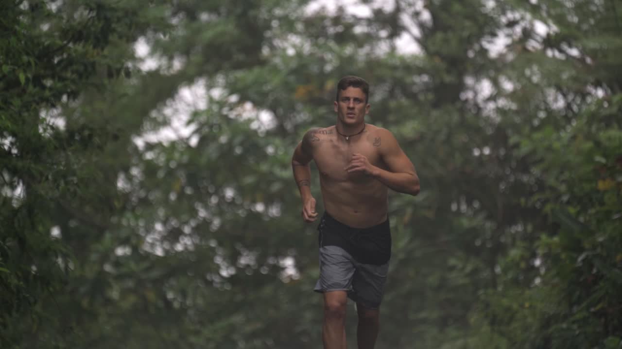 A shirtless man is captured mid-stride, running on a path surrounded by dense, green foliage