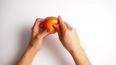small orange citrus in hands. woman's hands cleaning mandarin neatly on white background. top view.