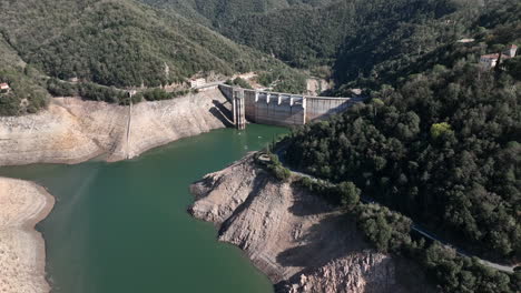 Luftaufnahme,-Die-Den-Staudamm-Des-Leeren-Sau-Sumpf-Reservoirs-Mit-Dem-Sonnendurchfluteten-Katalanischen-Waldtal-Umkreist