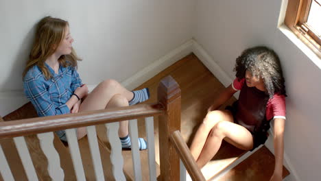 sad diverse female friends sitting on stairs and talking at home, slow motion