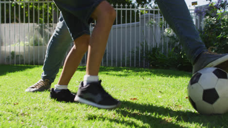 sección media de un hombre biracial y su hijo jugando al fútbol en el jardín