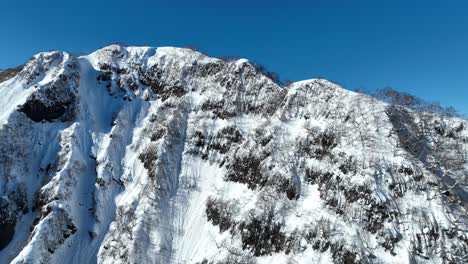 Aerial-wide-establishing-orbiting-ascending-shot-of-Japan's-mount-myōkō,-on-a-clear-winter-day,-a-volcanic-mountain-in-Myoko-Togakushi-Renzan-National-Park-region