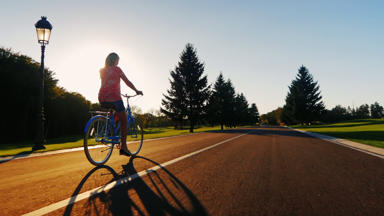 일몰에서 자전거를 타는 젊은 여성은 슬로우 모션 비디오를 다시 봅니다.