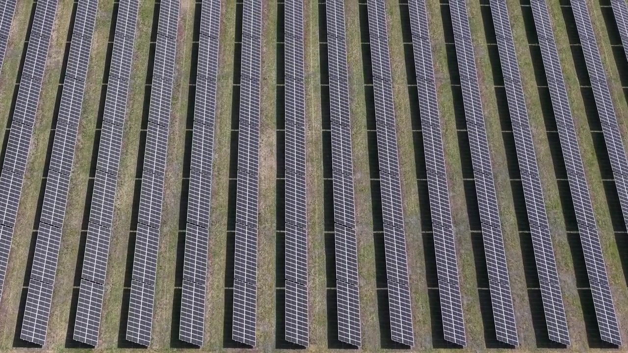 Una vista aerea dall'alto cattura un grande impianto solare con centinaia di pannelli fotovoltaici disposti in file parallele, che rappresenta la produzione di energia sostenibile.
