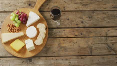 vídeo de quesos, pan, uvas y nueces a bordo y vino tinto en una mesa de madera, con espacio para copiar