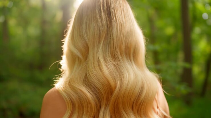 Donna caucasica bionda di spalle in una foresta con lunghi capelli mossi illuminati dalla luce dorata del sole, scena estiva serena