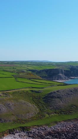 vertical video of welsh landscape with cliffs above calm ocean in gower with views of fall bay and mewslade bay as rhossili rural village comes into picture.