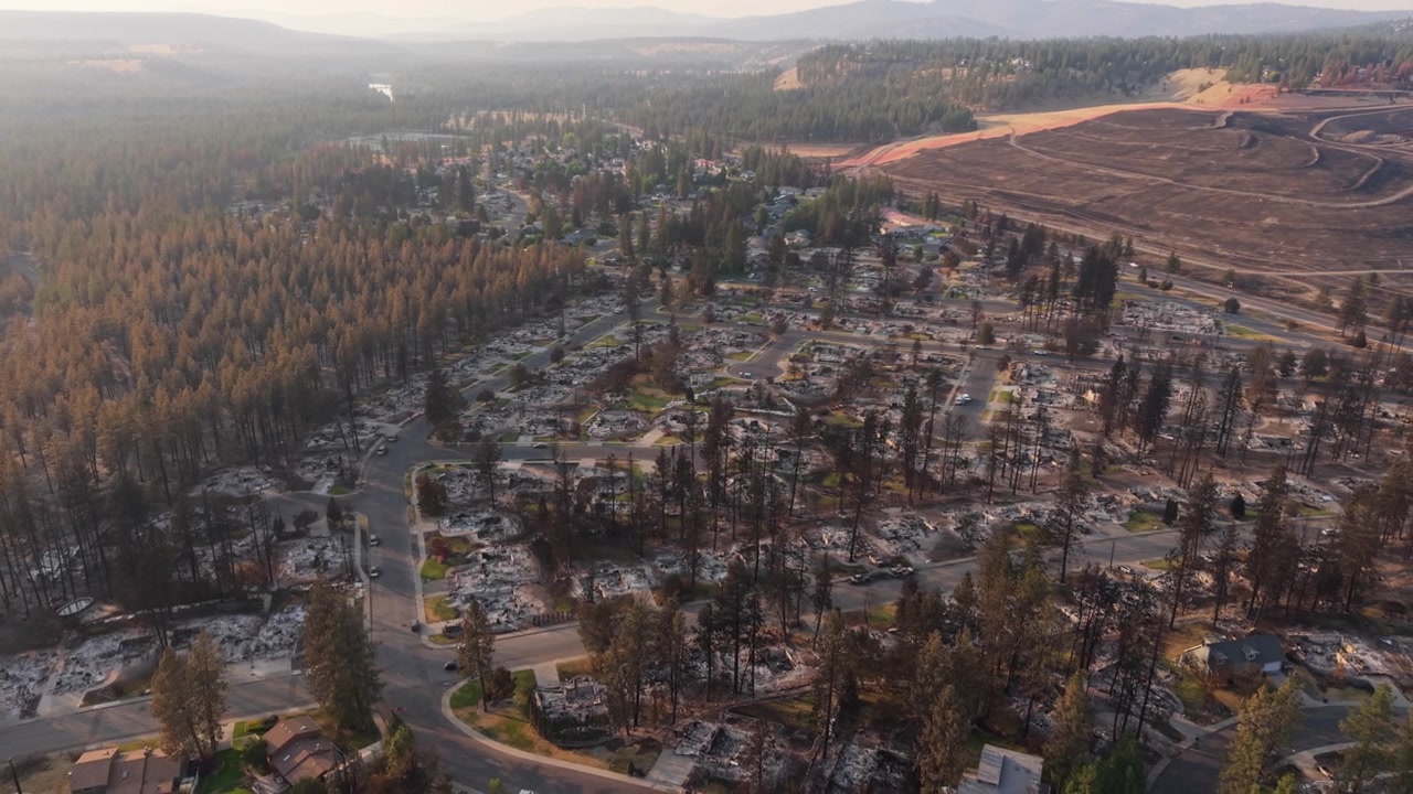 Spokane Old Trails Fire damage shown in a slow backward wide shot over a burned neighborhood, with destroyed homes and charred lots glowing in warm sunset light.