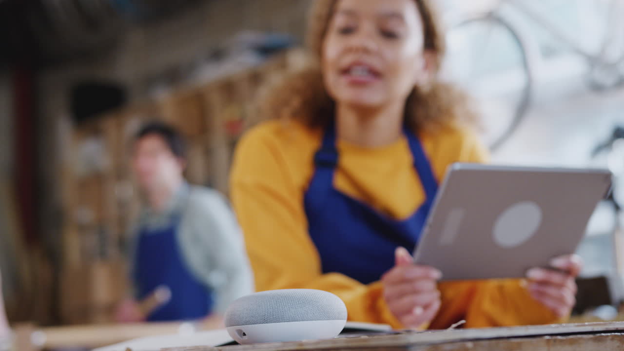 Vrouwelijke werknemer in een timmerwerkplaats die een digitale tablet gebruikt en een vraag stelt aan een slimme luidspreker.
