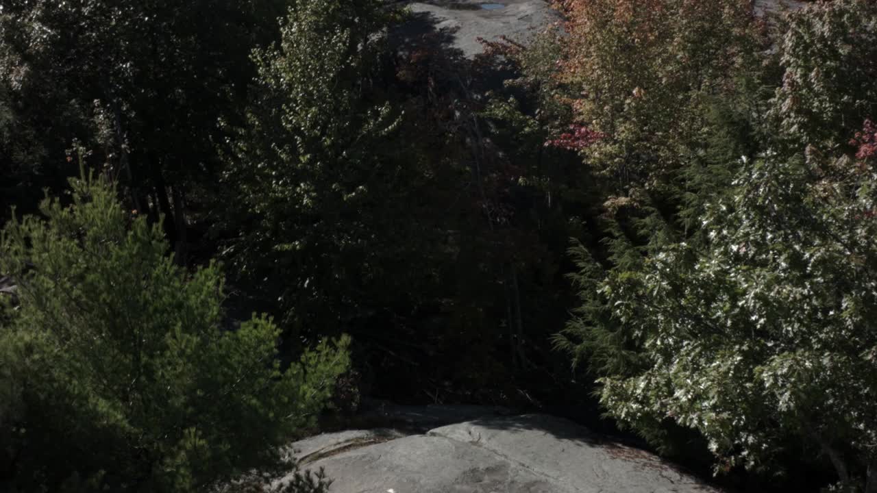 una toma inclinada de grandes rocas en la ladera de una montaña revela montañas y bosques distantes en la distancia
