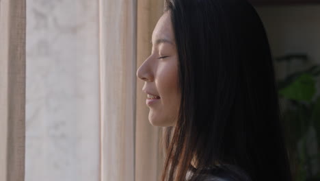 beautiful asian woman opening curtains looking out window ready for fresh new day feeling rested