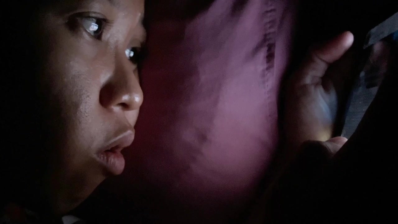 Primo piano estremo al rallentatore di profilo del viso di una donna illuminato dallo schermo di uno smartphone mentre è sdraiata a letto di notte. Concetto di dipendenza dalla tecnologia a tarda notte e tempo trascorso davanti allo schermo prima di dormire.