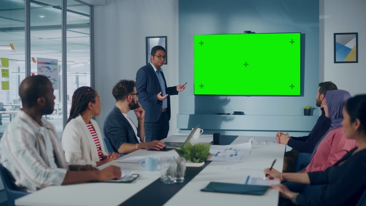 Office Conference Room Meeting Presentation: Indian Businessman Talks, Uses Green Screen Chroma Key Wall TV. Digital Entrepreneur Presenting a Product to Group of Multi-Ethnic e-Commerce Investors