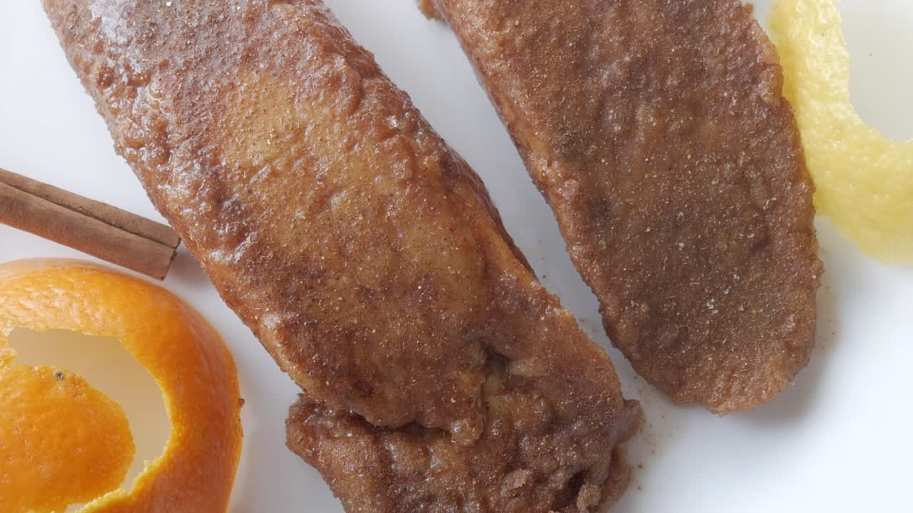 Golden brown Spanish torrijas with cinnamon, orange zest, and syrup on a white plate
