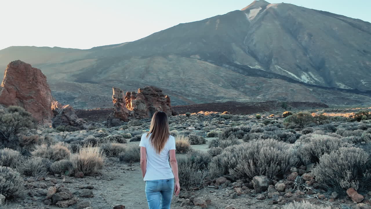 Viaggiatrice che cammina su un sentiero in una splendida valle vulcanica con il vulcano Teide sullo sfondo durante una giornata di sole