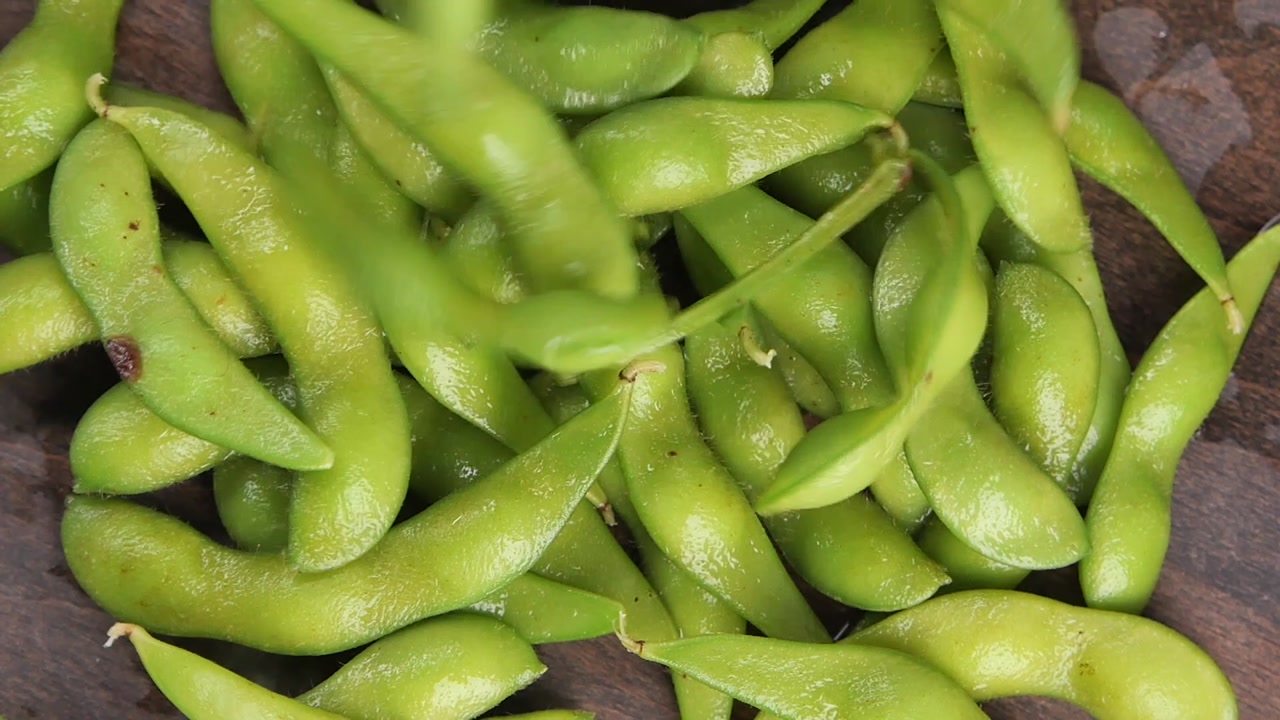 Fresh Edamame Pods Falling onto a Wooden Surface