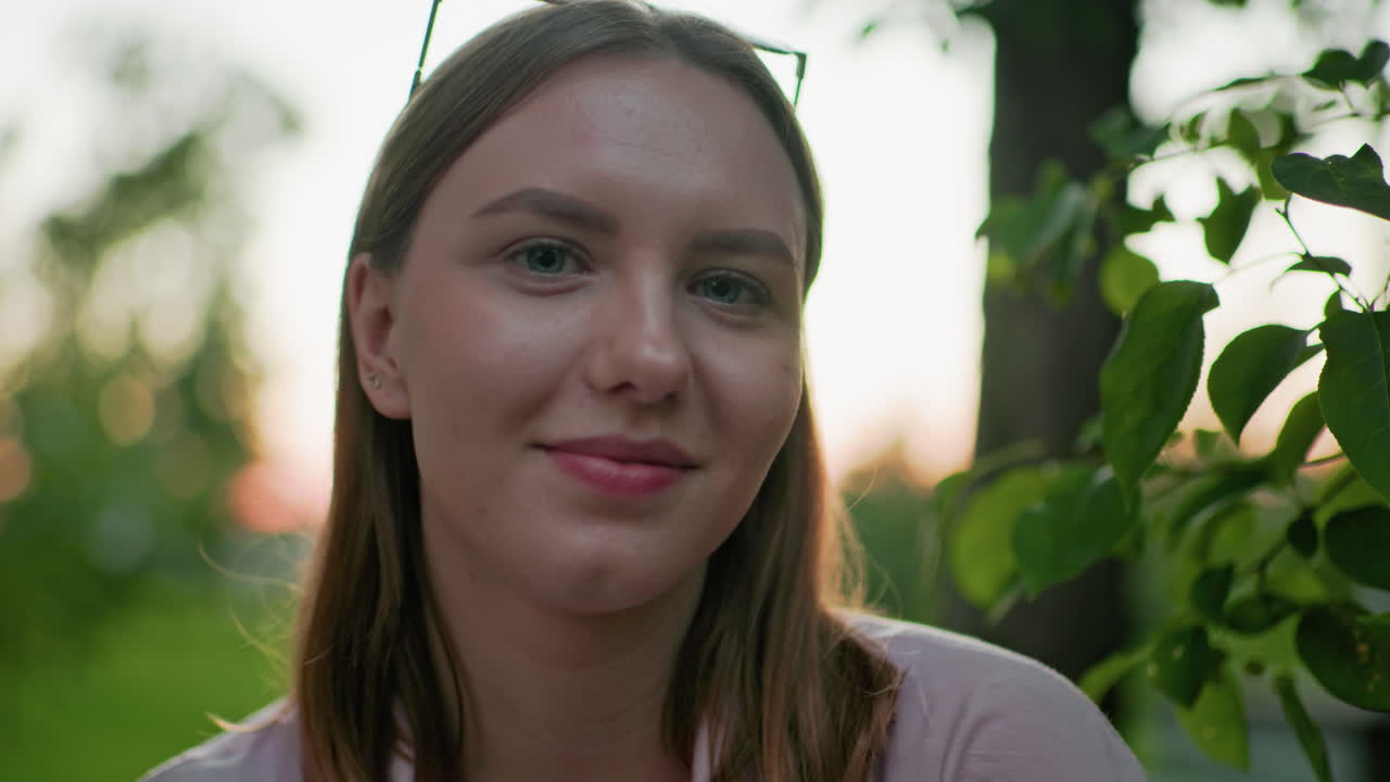 primer plano de una mujer con una cálida sonrisa, rodeada de árboles verdes y una suave iluminación exterior, creando una atmósfera serena en un entorno natural, perfecto para el estilo de vida