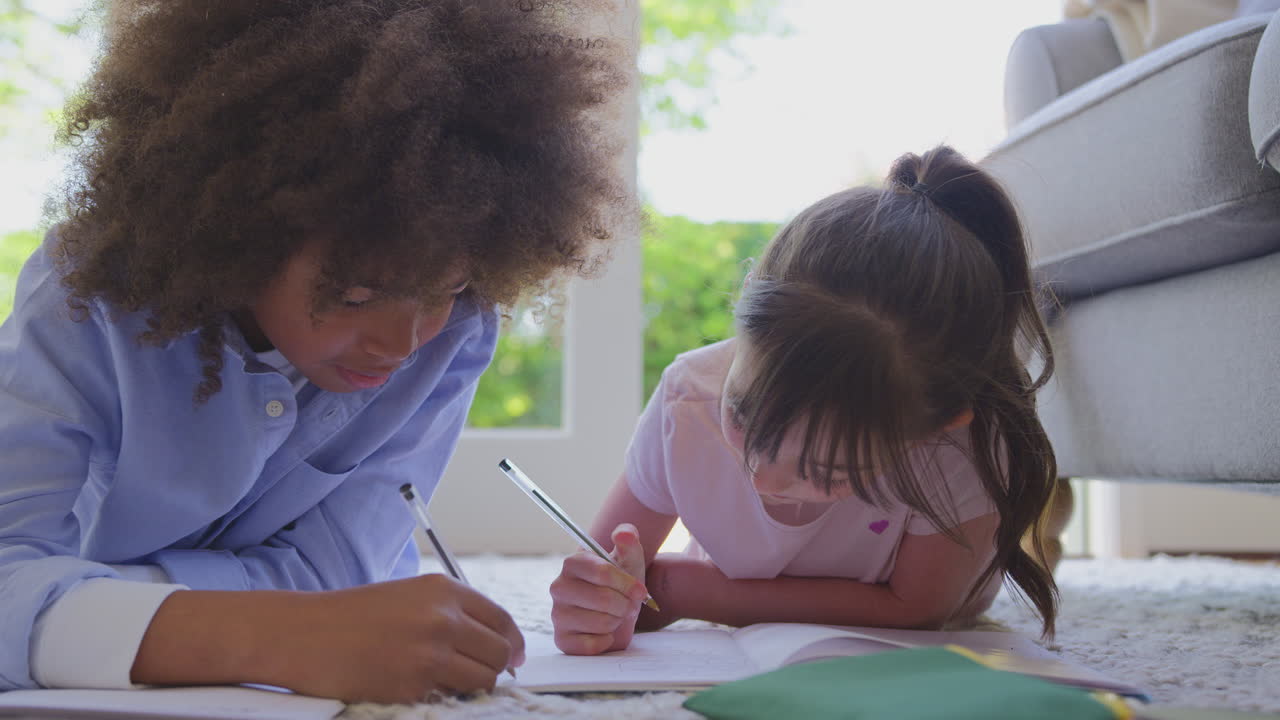 niño y niña acostados en la alfombra en el salón en casa haciendo la tarea escolar juntos