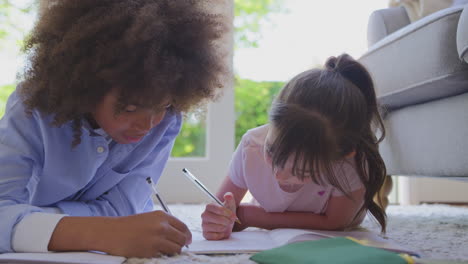 boy and girl lying on rug in lounge at home doing school homework together