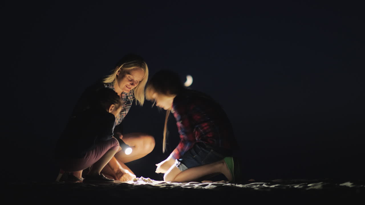 늦은 저녁 해변에서 모래사장에서 놀고 있는 두 딸과 함께 엄마는 위스콘신에 불을 붙입니다