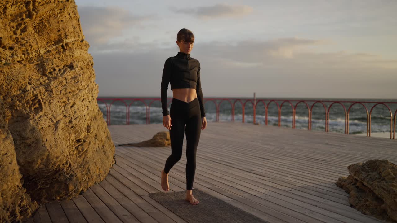 Woman practicing yoga on a wooden platform by the beach during sunset