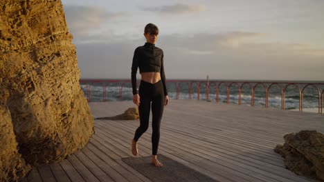 mujer practicando yoga en una plataforma de madera junto a la playa durante el atardecer