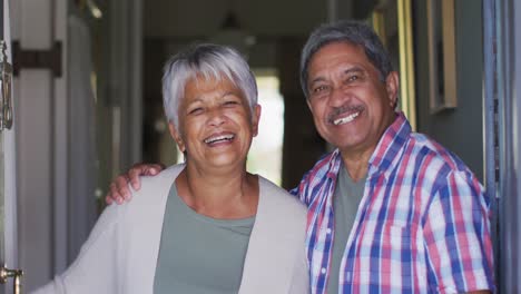 Senior-mixed-race-couple-standing-in-open-front-doorway-smiling-to-camera