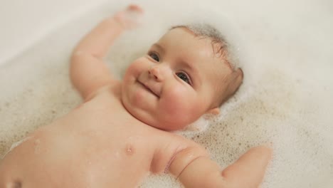 side view portrait of a little girl lying on her back in a large bath with foam