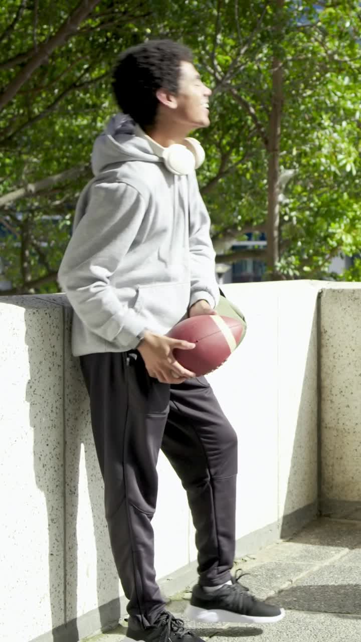 Vertical video: Donning headset, gray hoodie man greeting friend coming on roof, tossing football