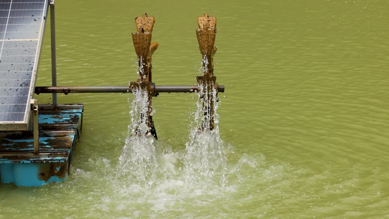 Un aeratore a ruota idraulica alimentato a energia solare funziona su uno stagno, mostrando l'uso di energia sostenibile e il movimento dell'acqua.
